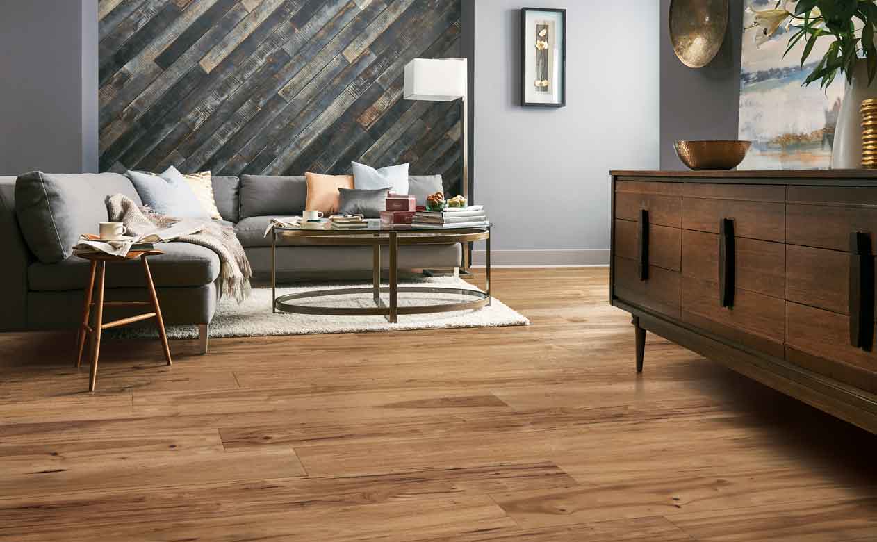 midtone hardwood flooring in living room with gray plank walls and gray couch